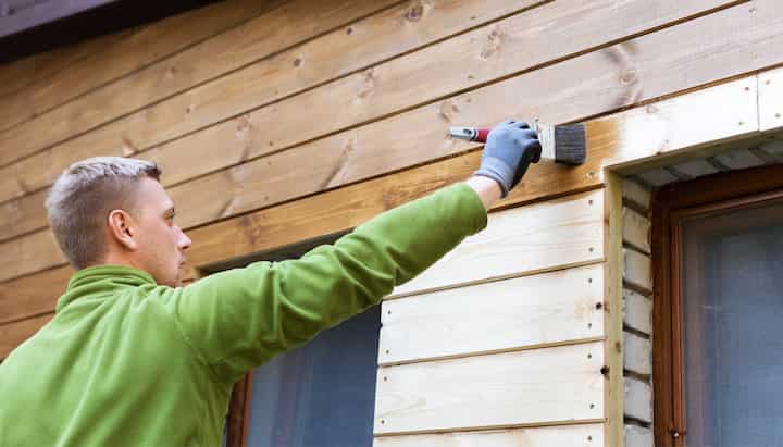 A professional painter using a long-handled brush to apply paint to the exterior of a house in Frederick.